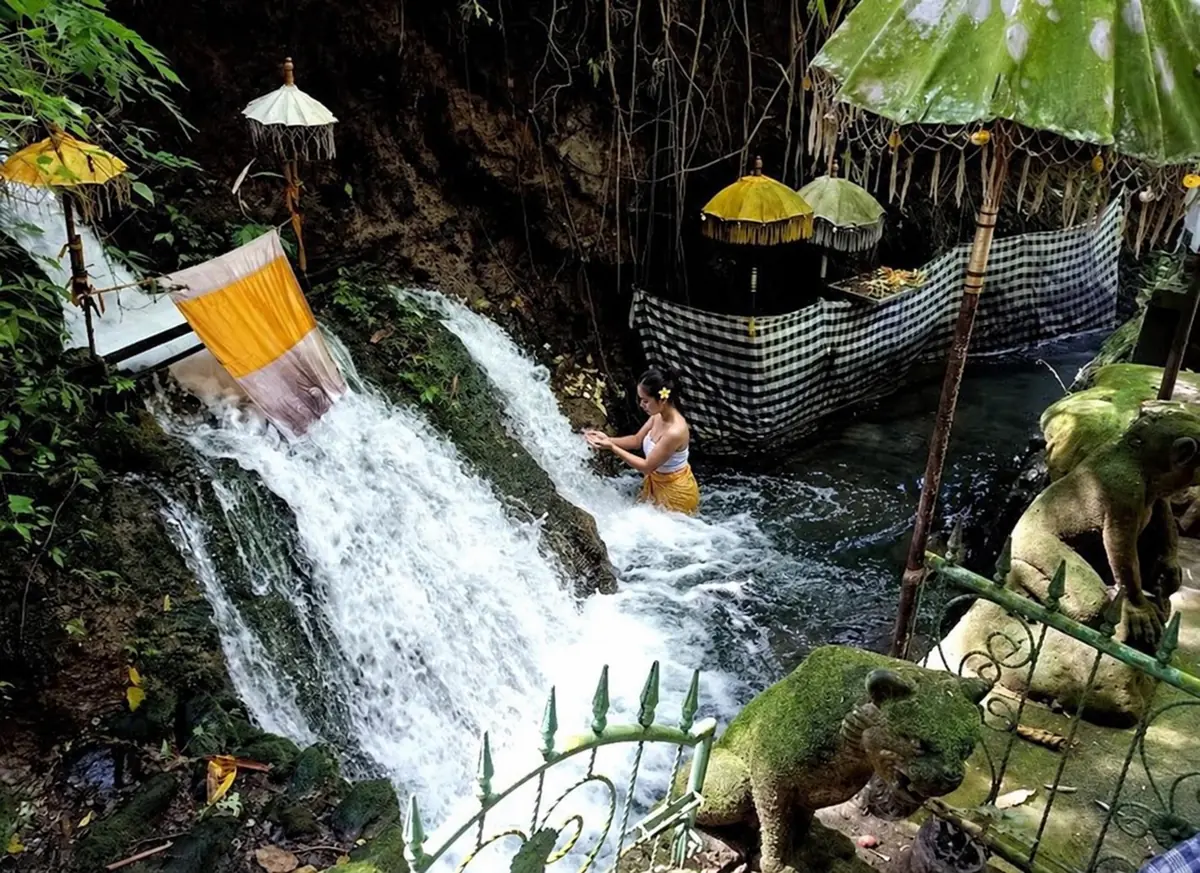 Woman taking part in melukat beside flowing water and Balinese shrines in Sebatu.